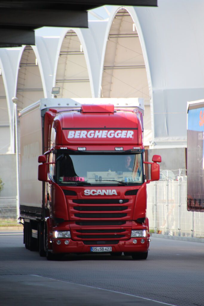 Ein roter LKW von Berghegger fährt durch ein Gewerbegebiet.