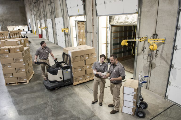 Uniformed warehouse workers loading boxed products into truck in a distribution warehosue.