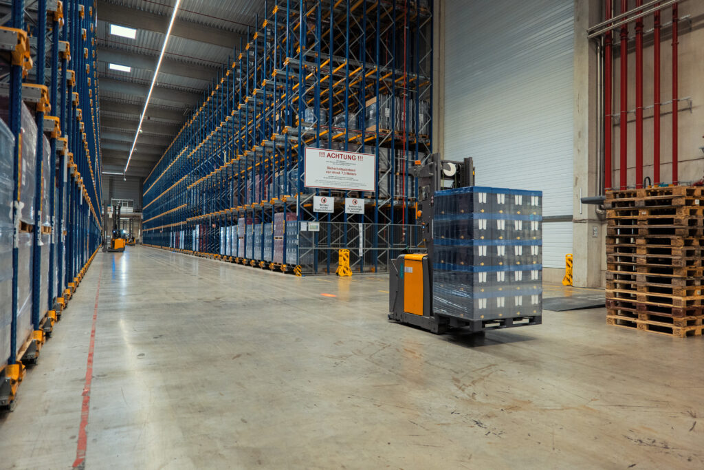 Zwischen breiten Hochregalreihen bewegen sich Fahrerlose Transportsysteme und transportieren Paletten in einem automatischen Logistik-Lager.