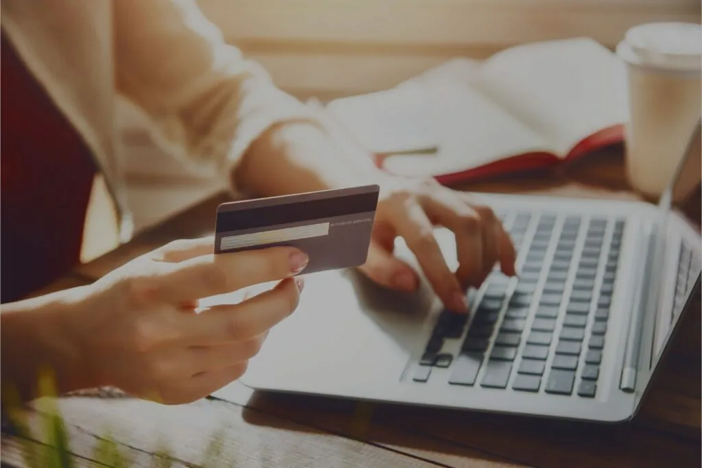 Eine Frau bestellt etwas online über ihr Laptop, in der rechten Hand hält sie eine Kreditkarte.
