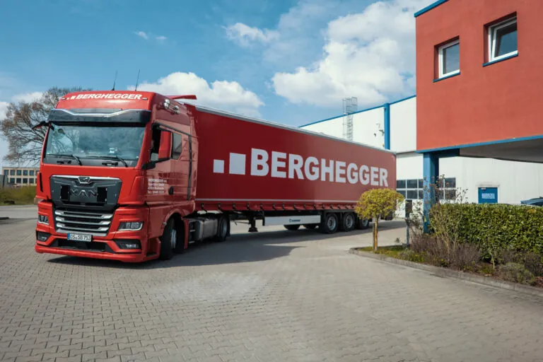 Ein roter LKW von Berghegger, ein Unternehmen der Maintrans Gruppe, vor dem Berghegger Firmensitz.