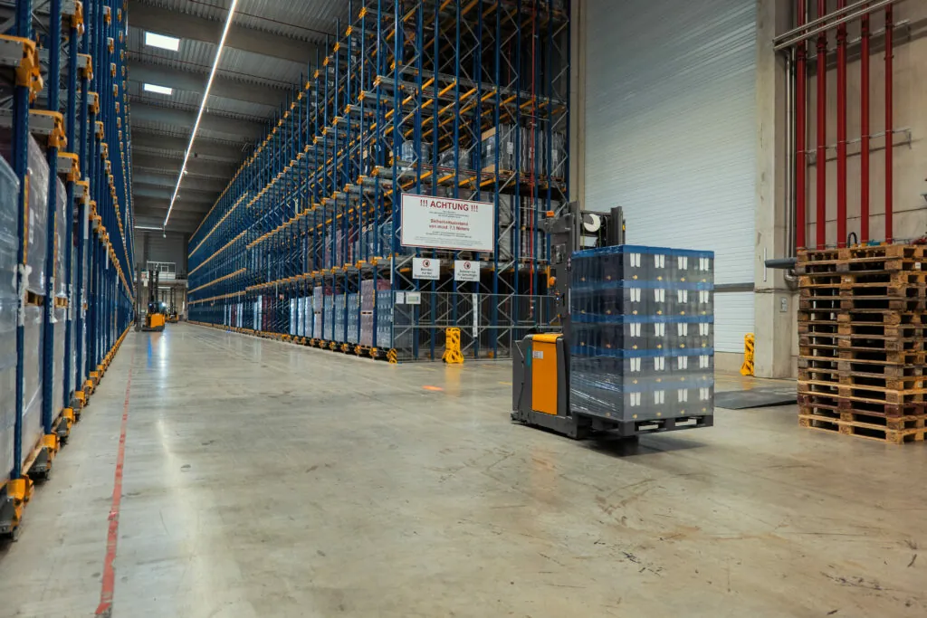 Zwischen breiten Hochregalreihen bewegen sich Fahrerlose Transportsysteme und transportieren Paletten in einem automatischen Logistik-Lager.