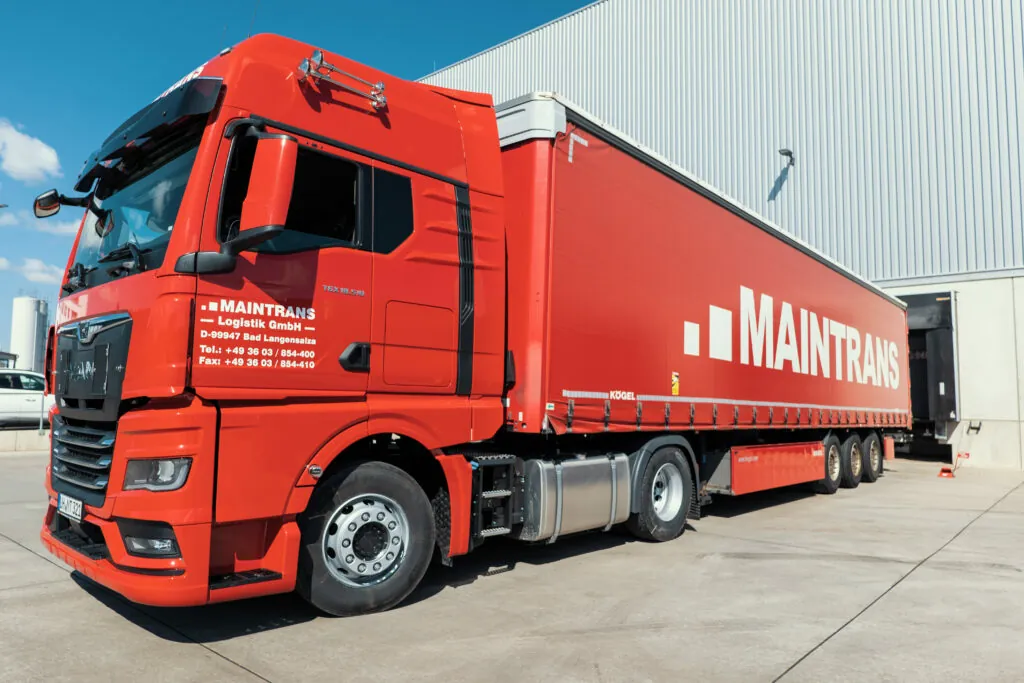 Roter Maintrans-LKW mit Maintrans-Logo steht an der Laderampe eines Logistik-Lagers.