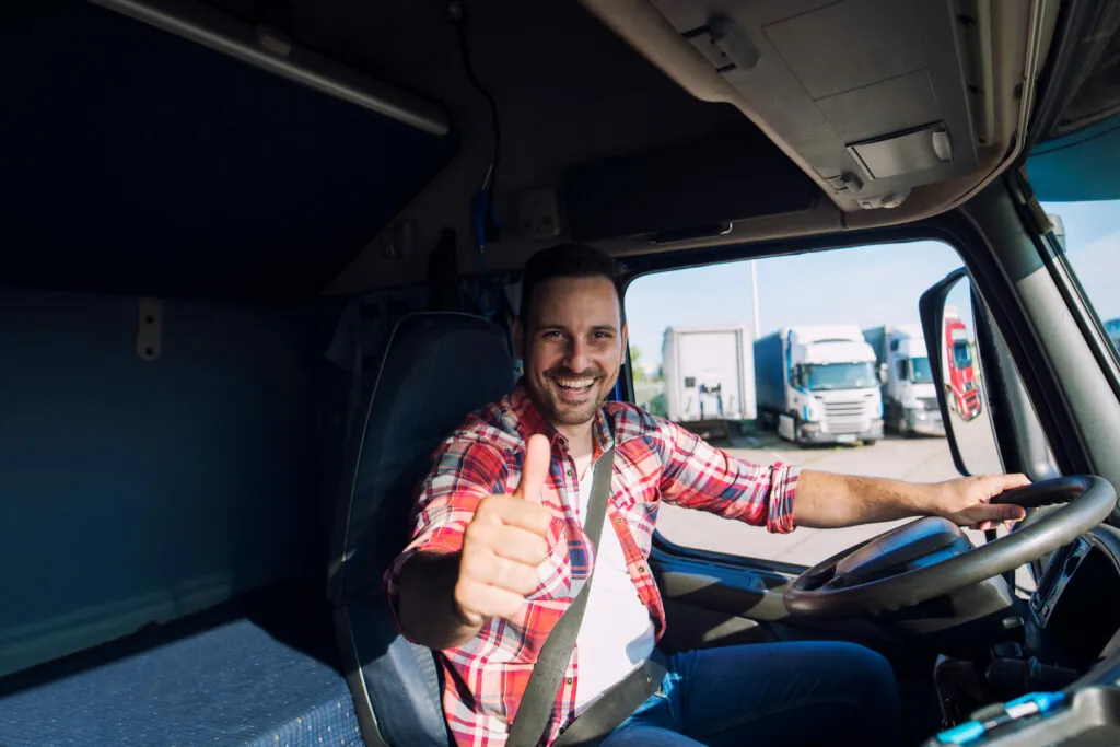 Ein LKW-Fahrer lächelt aus seiner Fahrerkabine und zeigt den Daumen hoch.