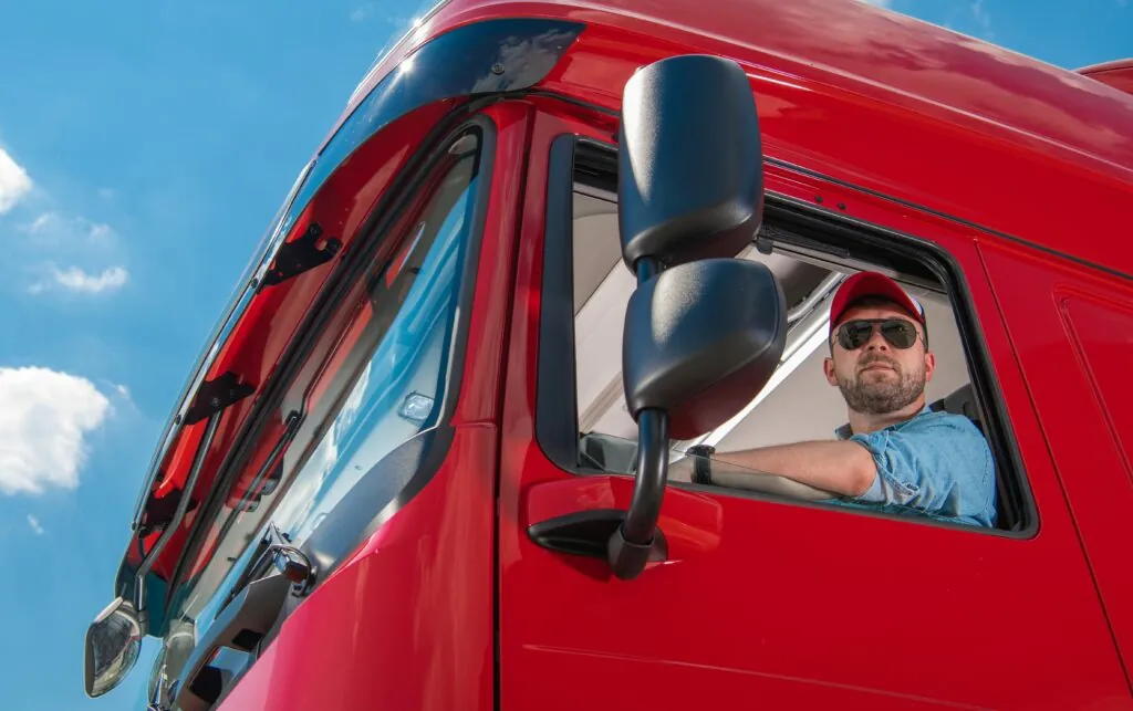 Ein LKW-Fahrer schaut aus dem Fenster seines roten LKW.