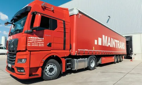 Roter Maintrans-LKW mit Maintrans-Logo steht an der Laderampe eines Logistik-Lagers.